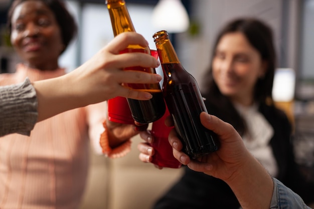 Office colleagues making toast and clinking glasses of alcohol, having drinks after work hours. Cheerful people enjoying champagne, wine or beer, doing cheers symbol at party. Close up.