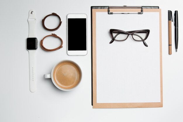 Office desk table with cup, supplies, phone on white surface