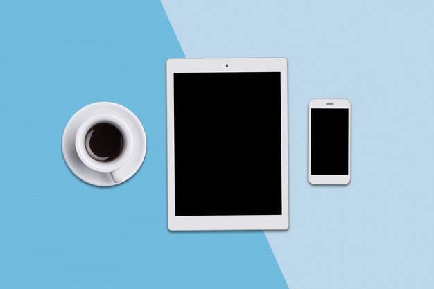 Office desk with modern tablet, smart phone and cup of coffee. View from above of modern gadgets lying on blue. Modern technologies, communication, occupation and office work concept