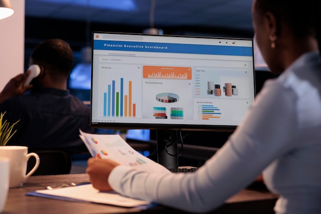 Office employee analyzing business charts on computer and documents, looking at online research data to create presentation. Working with information on report, statistics on pc.