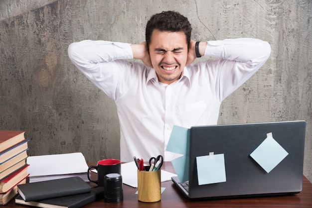 Free photo office employee holding his ears at the office desk.