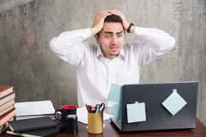 Free photo office employee holding his head with much work at the office desk.