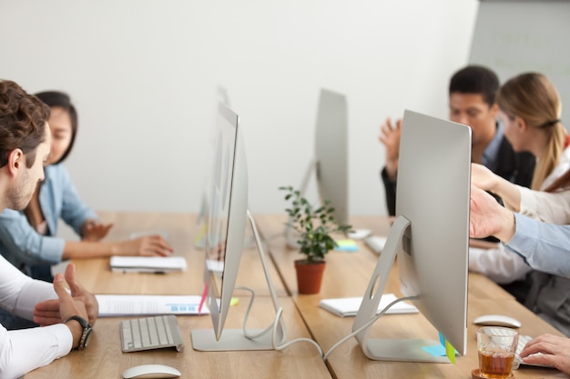 Office employees working on computers in coworking, desk with monitors