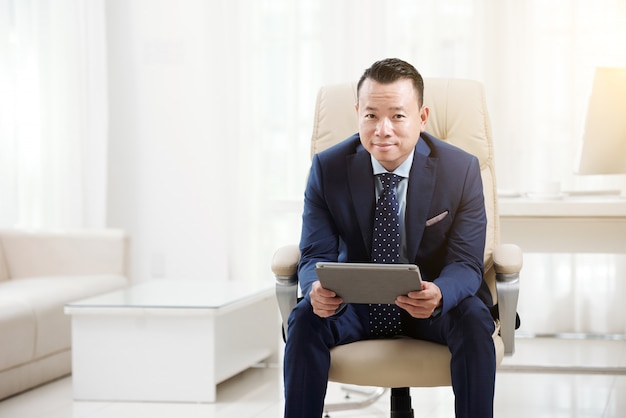 Free photo office manager relaxing in his chair with digital pad looking at camera