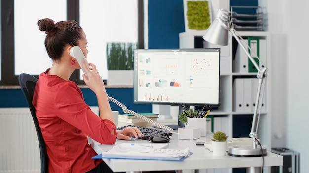 Office secretary using landline phone to talk about work, having remote conversation to create business growth. Female employee answering telephone call in startup company office.