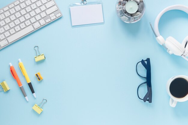 Office supplies; keyboard; coffee cup; card; eyeglasses; candle and headphone on blue background