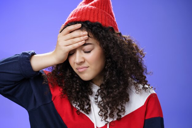 Oh god why me. Portrait of pissed and irritated fed up cute girl with curly hair looking down with regret and disappointed making facepalm gesture from annoyance being bothered by stupid question.