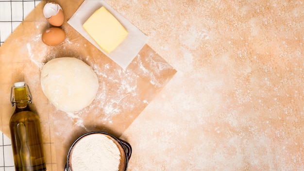 Oil bottle; flour; butter block; eggs and ball of dough on kitchen counter