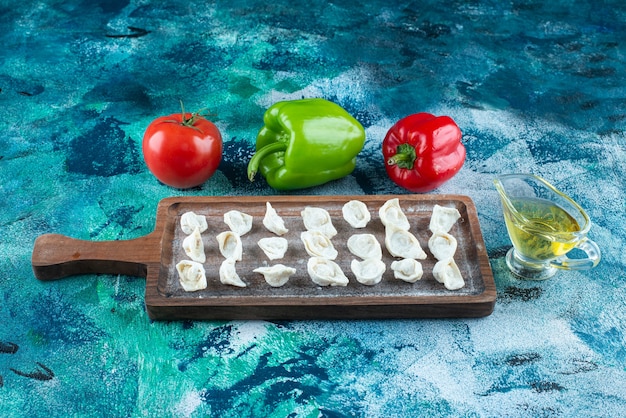 Oil and vegetables next to Turkish ravioli on a board , on the blue table. 