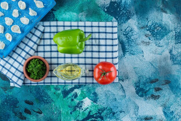 Oil and vegetables next to Turkish ravioli on a board on the tea towel, on the blue table. 