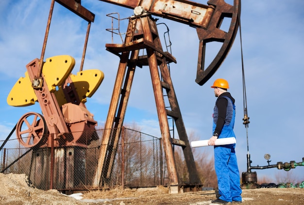 Нефтяник стоит на месторождении рядом с насосной станцией с большой бумагой