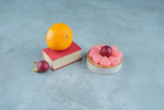 OIrange on a book, marmelades on a wooden piece and two decorative balls on marble.