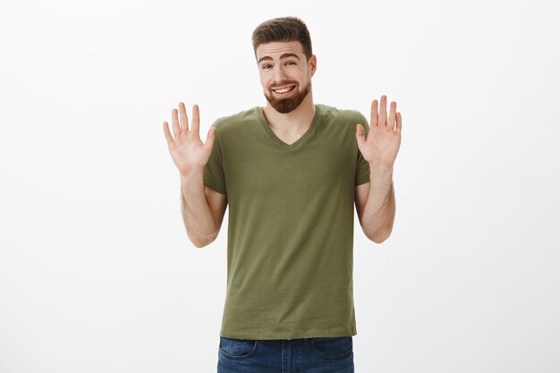 Okay calm down I am sorry. Portrait of handsome cute young bearded man feeling awkward apologizing for refusal raising hands in surrender with silly smile making accuses and rejecting offer