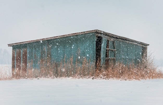 Free photo old abandoned wooden blue hut in a deserted area during the snow storm