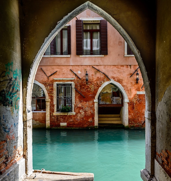 Old arch near the canal and an ancient red house with open windows