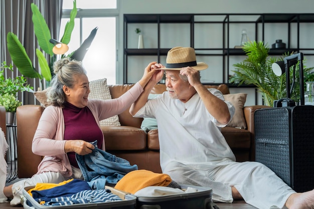 Old asian senior couple packing cloth and stuff for a trip togetherhappiness asian old age retired mature adult enjoy arrange cloth together on floor at living room at home interior background