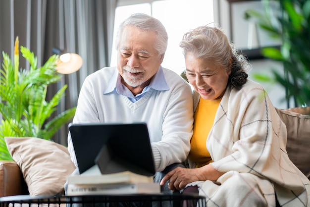 노년 아시아 노인 부부는 소파 소파에 앉아 태블릿 장치 소셜 연결 가정 격리를 통해 가족과 화상 통화를 하고 집 상태를 유지합니다.