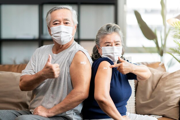 フェイスマスクウイルス保護の幸福を身に着けている古いアジアの老夫婦は、手のジェスチャーポイントでワクチン接種され、ウイルス保護に自信を持っている陽気なショー包帯注射covid19