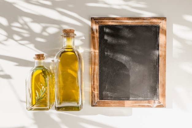 Free photo an old blank wooden frame slate with two oil bottles against the wall