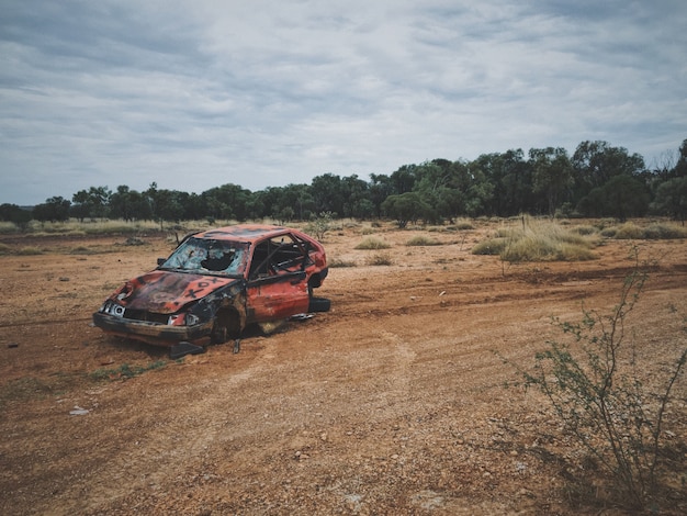 Old broken up car in a dry grass field with trees