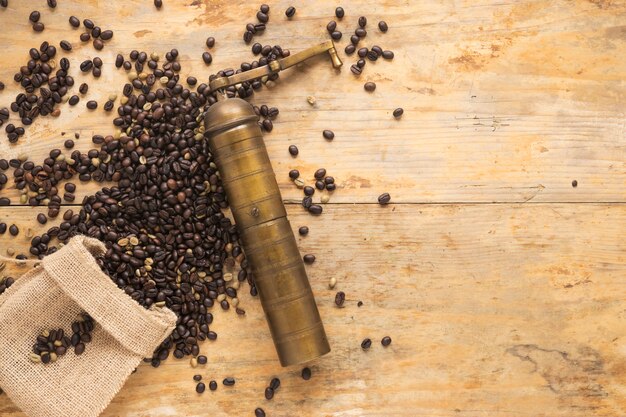 Old coffee grinder with coffee beans falling from sack on table