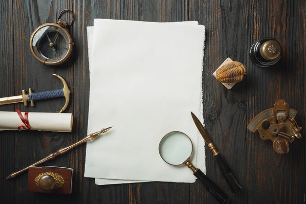 Old fashioned flat lay with letters writing accessories on dark wooden table. White sheets, pen, signet, package, ink. Vintage style, steampunk, gaslight concept. Magnifying glass and compass.