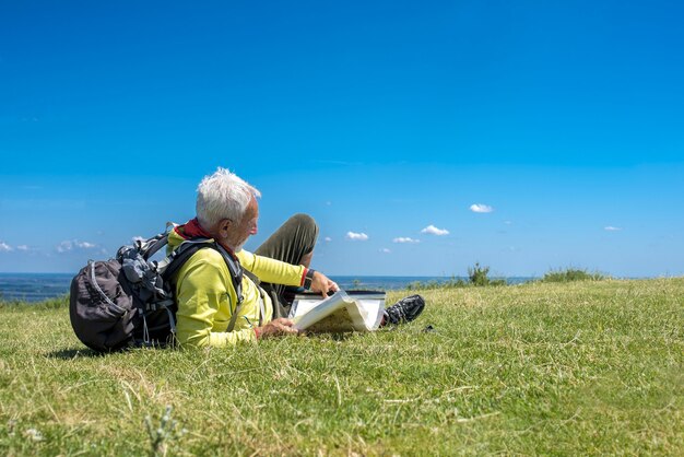 Старый мужчина-путешественник, лежащий на лугу и смотрящий на карту