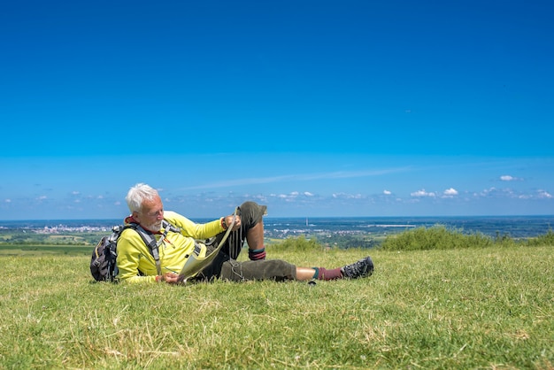 Free photo old male hiker lying in a meadow and looking at a map