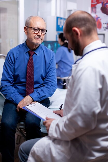 Old man answering doctor questionnaire during examination in hospital room