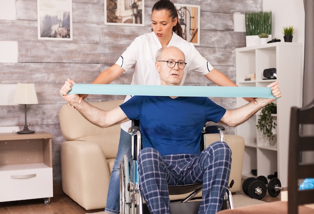 Старик делает упражнения на мышечную травму с помощью эспандера с медсестрой рядом