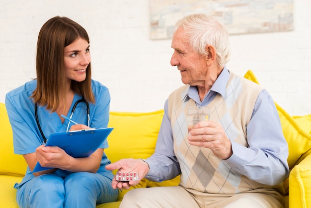 Old man holding his pills while talking to a nurse