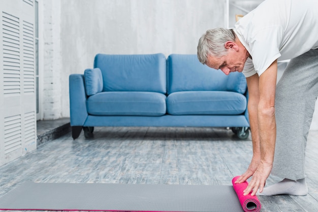 Old man rolling yoga mat on floor