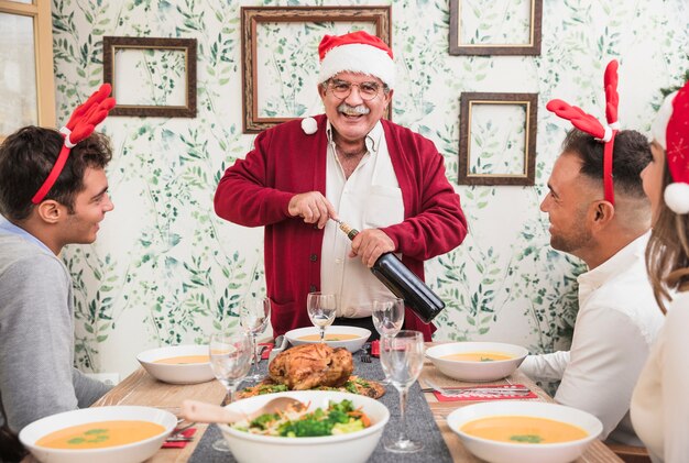 Старик в шляпе Санта, открывая бутылку вина на праздничном столе