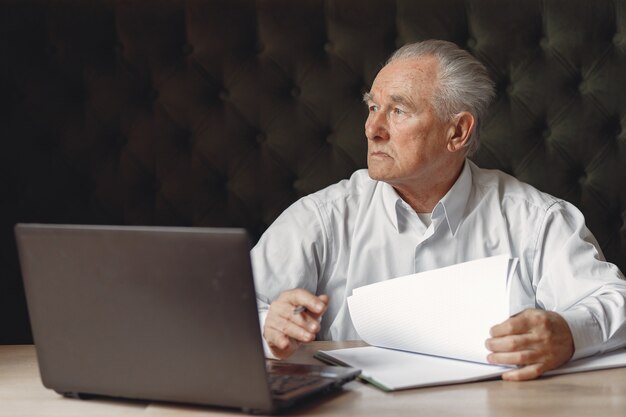 Old man sitting at the table and working with a laptop