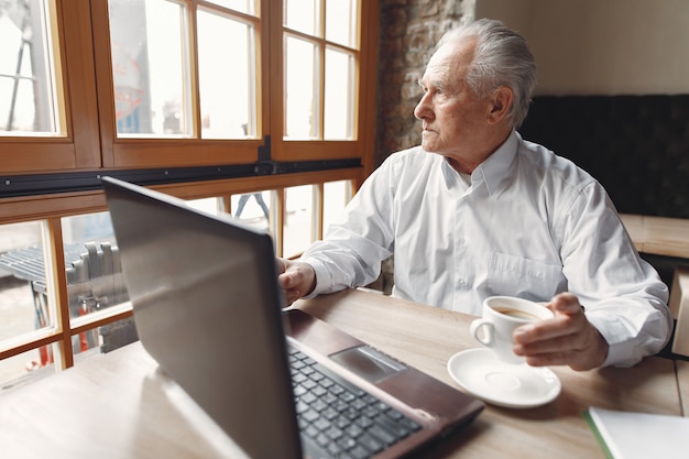 Old man sitting at the table and working with a laptop