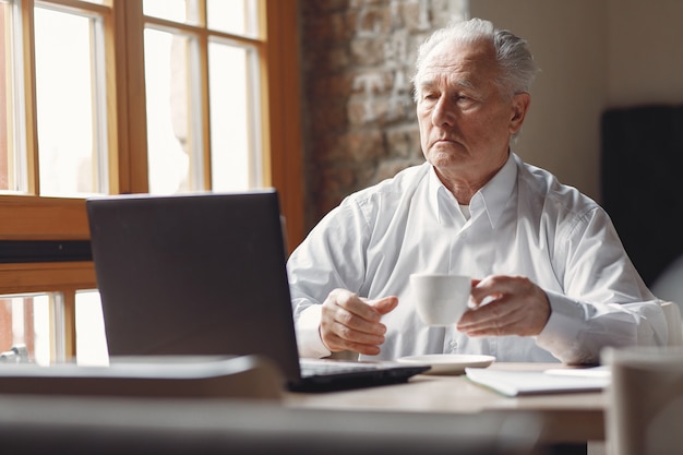 Old man sitting at the table and working with a laptop