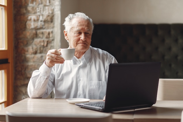 Old man sitting at the table and working with a laptop
