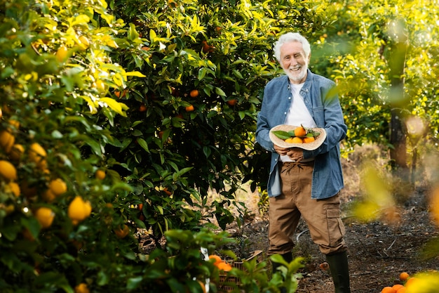 屋外で彼のオレンジの木の隣に立っている老人