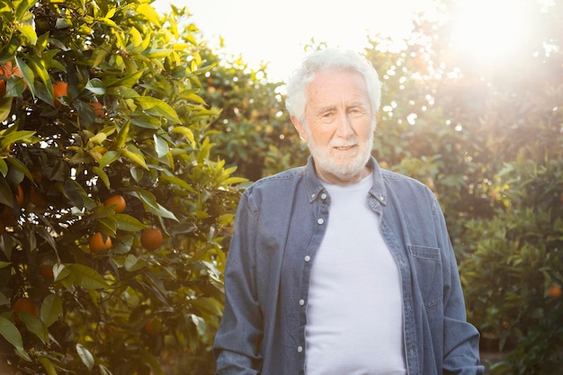 Foto gratuita il vecchio uomo in piedi accanto ai suoi alberi di arancio all'aperto