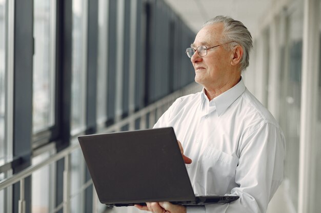 Old man standing in the office with a laptop