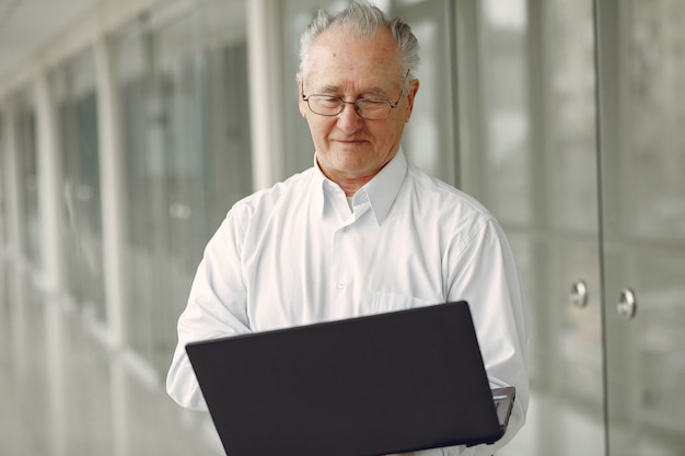 Old man standing in the office with a laptop