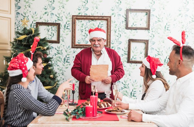 Old man standing with paper at festive table 