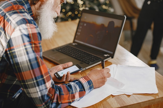 Old man with laptop. Grandfather sitting in a Christmas decorations. Man with mobile phone.