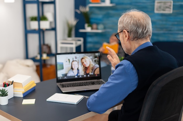 Старый родитель приветствует дочь во время видеоконференции на портативном компьютере