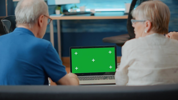 Пожилые люди с инвалидностью анализируют ноутбук с зеленым экраном. Пара на пенсии смотрит на шаблон пространства для копирования и изолирует макет с пустым хроматическим ключом на фоне компьютера. Современные технологии
