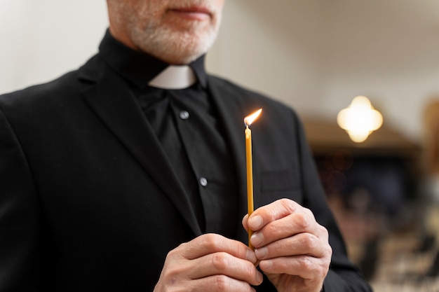 Старый священник держит свечу сбоку