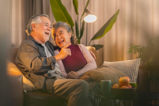Old retired age asian couple watching TV at homeold mature asian couple cheering sport games competition together with laugh smile victory on sofa couch at living room home isolation activity