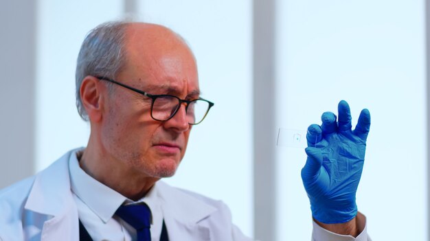 Old scientist man analysing virus sample in equipped laboratory. Scientist working with various bacteria, tissue and blood samples, pharmaceutical research for antibiotics against coronavirus pandemic