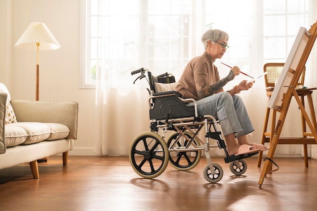 Old senior asian female tattoo using art therapy while his legs is injured at homeasian elder woman spend recovering of her leg is getting better with painting canvas art in living room at home