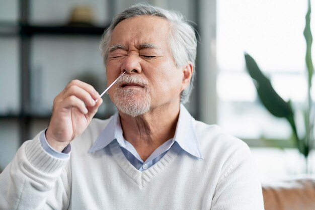 自宅でSARSco2ウイルスを検出するために自分で迅速なテストをテストする古いシニアアジア人男性の手の鼻腔スワブは、検疫の概念を分離します
